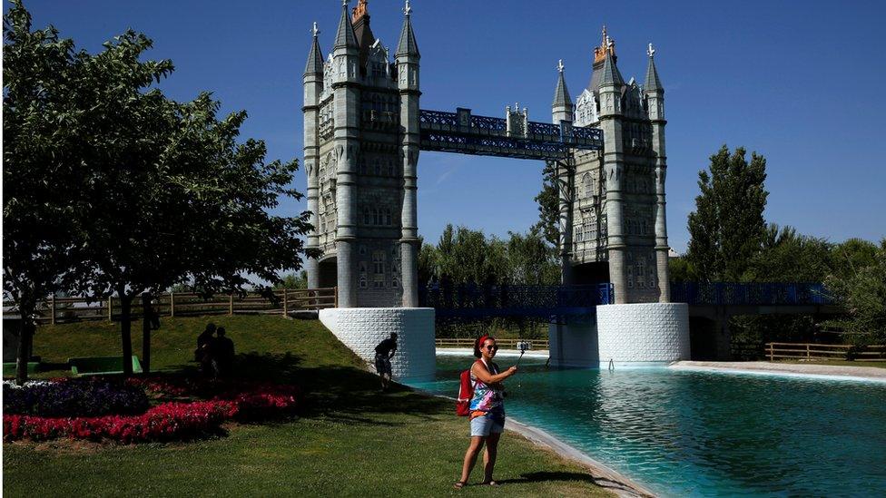 A woman taking a selfie in front of a replica of London's Tower Bridge