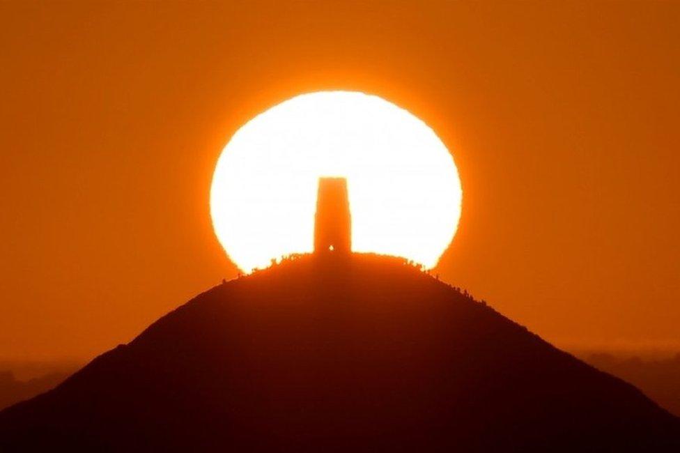 People standing around Glastonbury Tor in Glastonbury, as the sun rises.