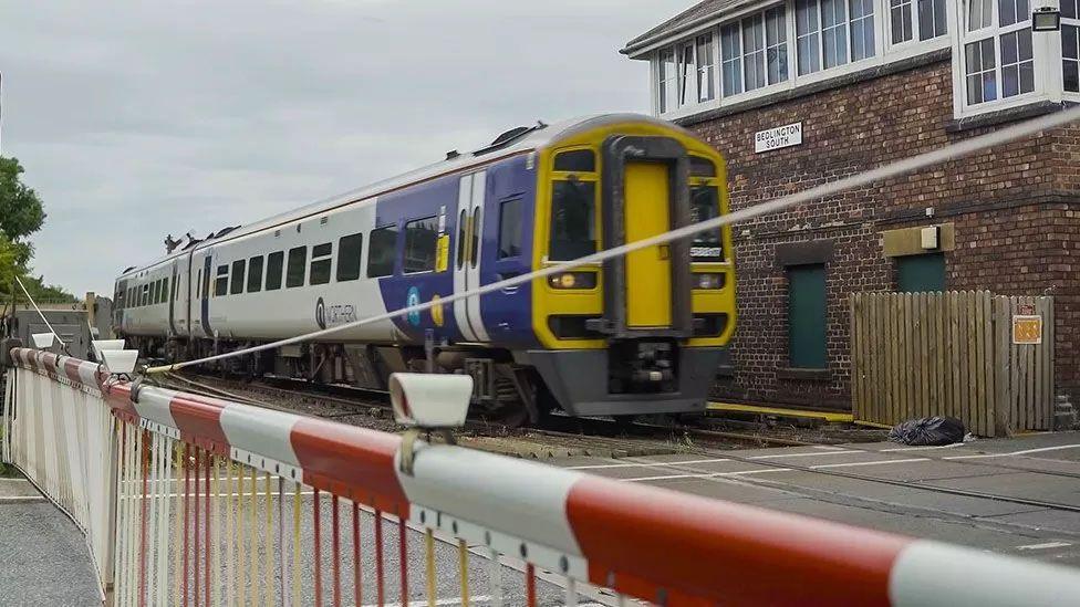 Train at station with level crossing barrier in the foreground