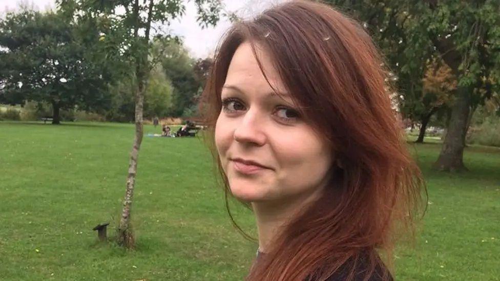 Yulia Skripal, pictured smiling at the camera in a park. She has long, dark red hair and is looking over her shoulder. 