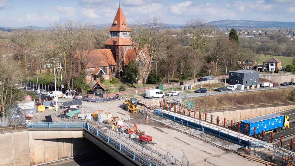 Church of St Anne, St Anne's Drive, Haughton, Denton, Greater Manchester. Exterior, view from north showing National Highways work to bridge on M67 to the south of the church