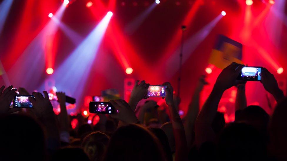 People with their arms up watching a music stage through their phones,