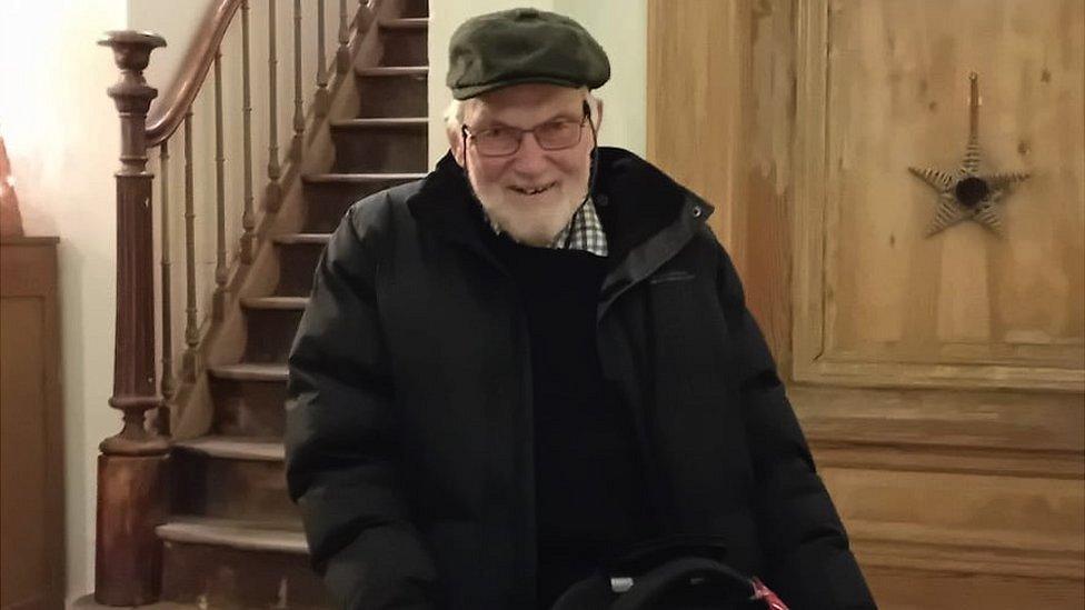 Image of Roger Sturge. He is wearing a black jacket and a green hat. He has a white beard and glasses. He is looking directly at the camera and smiling.