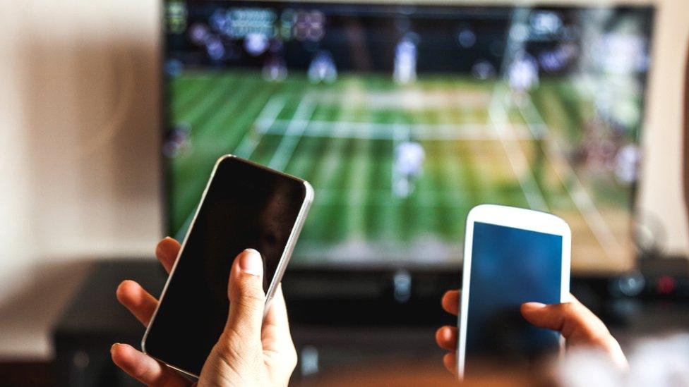 A pair of hands holding smartphones while watching tennis