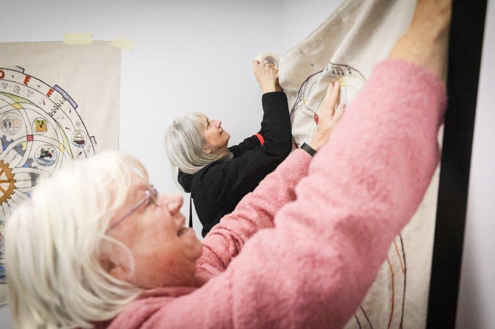 two stitchers hanging up a panel