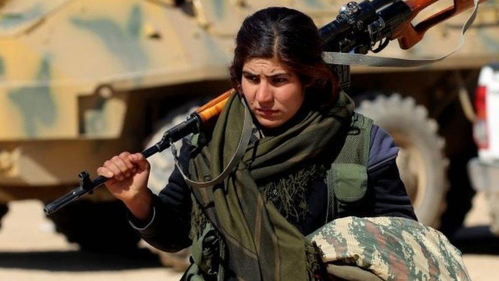 A female Kurdish fighter of the US-backed Syrian Democratic Forces (SDF), made up of an alliance of Arab and Kurdish fighters, walks carrying a weapon in the village of Sabah al-Khayr on the northern outskirts of Deir Ezzor as they advance to encircle the Islamic State (IS) group bastion of Raqa on 21 February 2017.