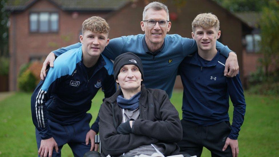 Two teenagers and a man stand behind a man in a wheelchair