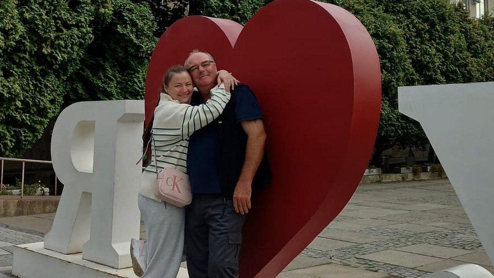 Steve and his fiancée hug in front of a large loveheart