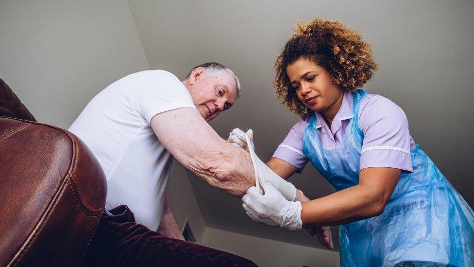 Library shot of carer in blue overall applying a bandage to an elderly man's arm