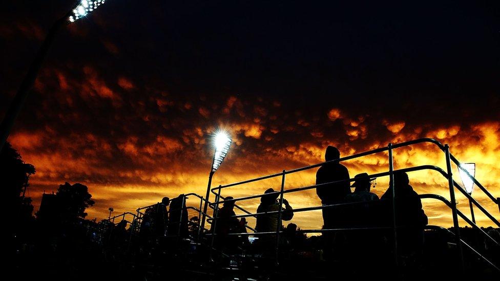 Cricket fans in a stand at Manuka Oval observe the sunset.