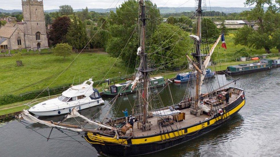 A tall ship sailing on a canal past a church