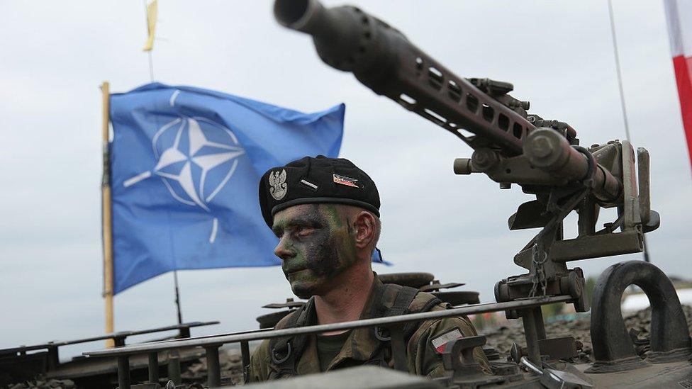 A soldier of the Polish Army sits in a tank as a Nato flag flies behind