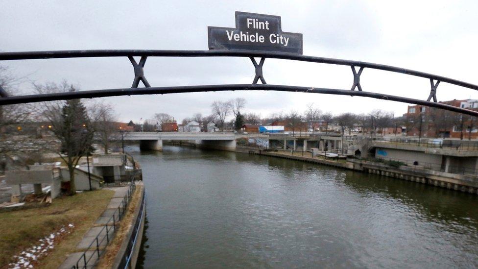 The file photo shows a sign over the Flint River noting Flint, Mich., as Vehicle City.