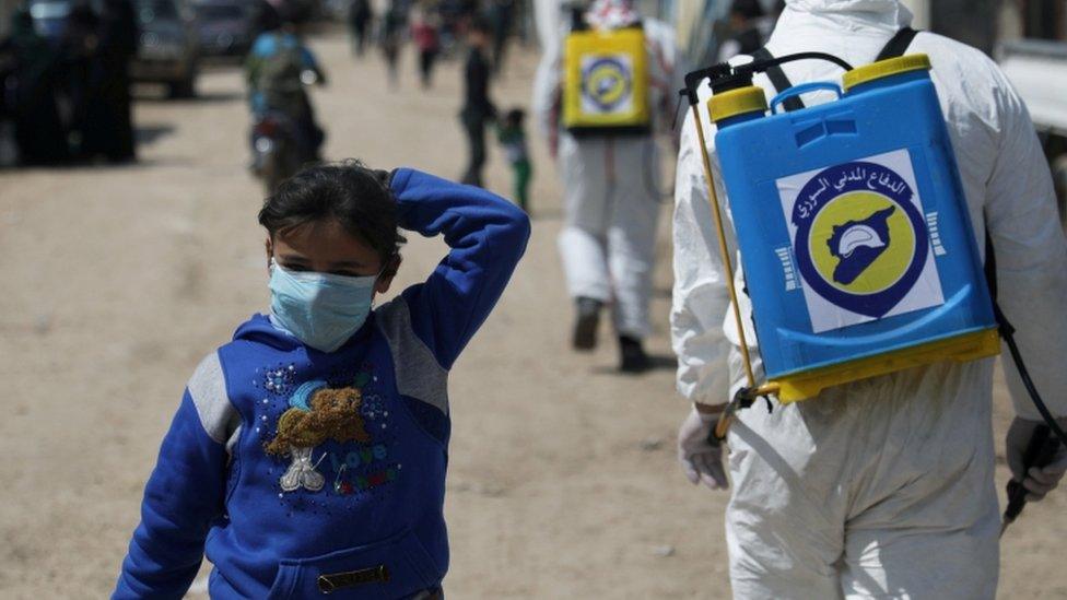 An internally displaced Syrian girl wears a face mask as members of the Syrian Civil defence sanitize the Bab Al-Nour camp