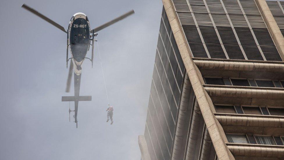 A man hanging from a helicopter during an operation to rescue a trapped firefighter - Johannesburg, South Africa