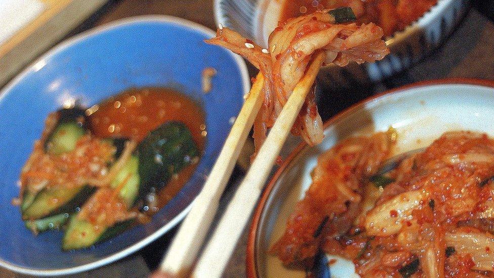 A close-up of chopsticks holding spicy traditional Korean pickles, kimchi