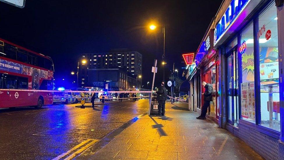 Night-time image showing a police cordon on the street outside Sutton station, with a bus and police cars in shot