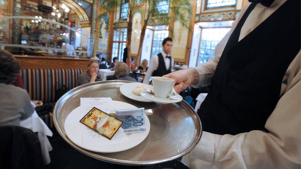 A waiter brings a coffee and the bill to clients at a restaurant in Nantes