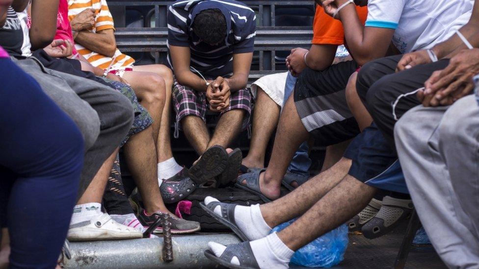 Suspected Mara Salvatrucha gang members sit in the back of a truck