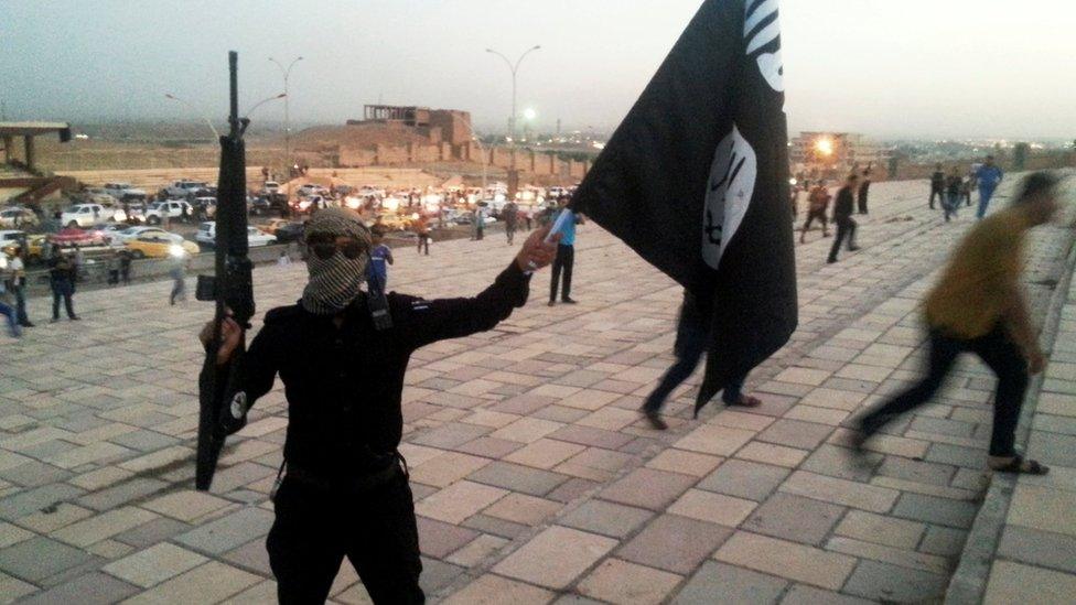 An Islamic State of Iraq and the Levant (ISIL) militant holds up a black banner and a rifle on a street in the city of Mosul on 23 June 2014