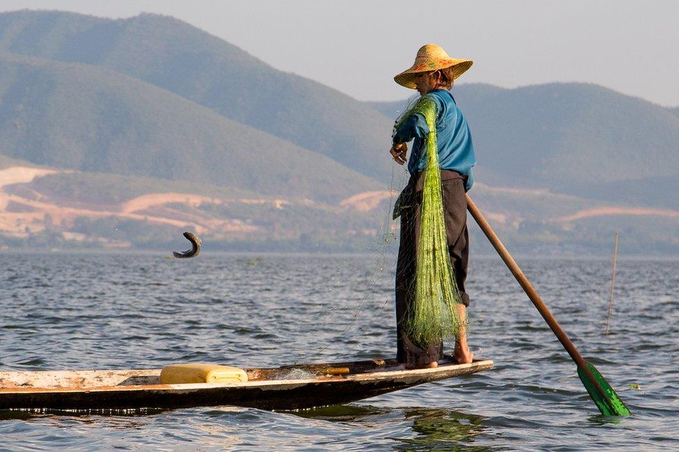 A fisherman tosses a fish on to his boat