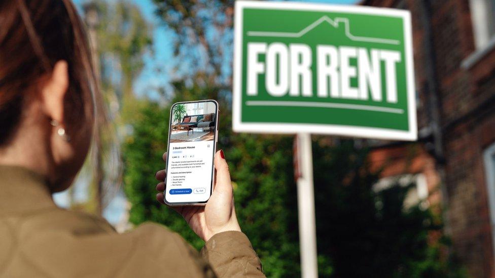 Woman looking at picture on phone outside building with For Rent sign