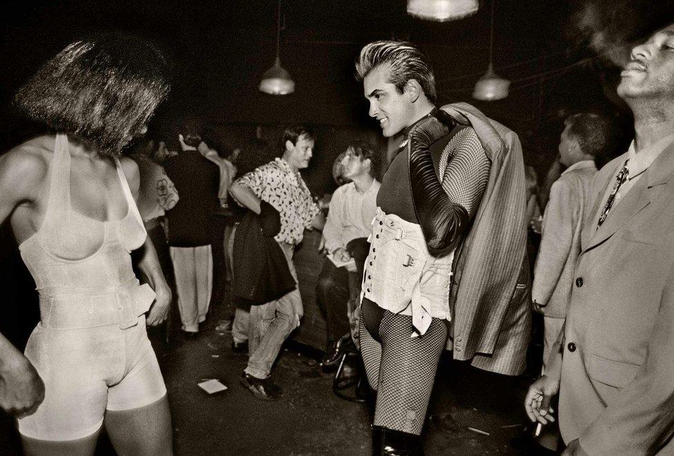 A man and a woman, both dressed in corsets, chat at a party