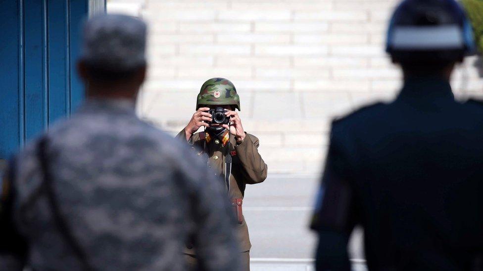 A North Korean army solider takes pictures as a South Korean and US army soldier stand guard at the border village of Panmunjom