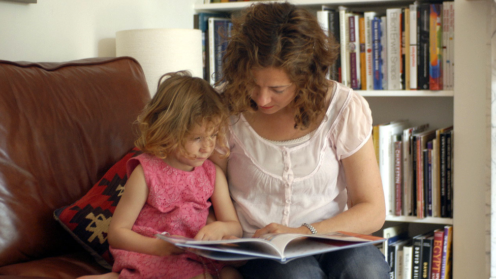 Three-year-old girl reading a book with her mother