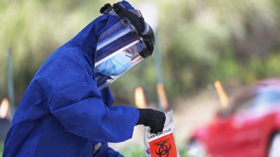 A volunteer carrying out drive-through testing, in full PPE, in California