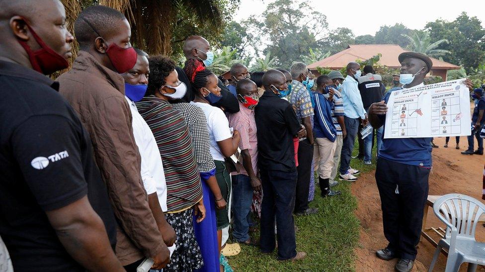 A man holds up a poster on how to mark a ballot paper as people queue at a voting center during the presidential elections in Kampala, Uganda, January 14, 2021.