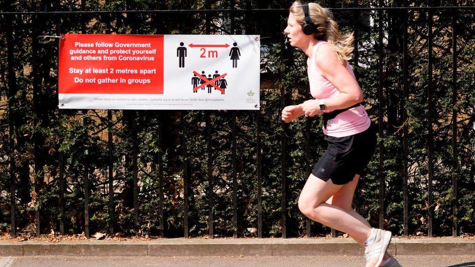 A runner running past a poster about social distancing