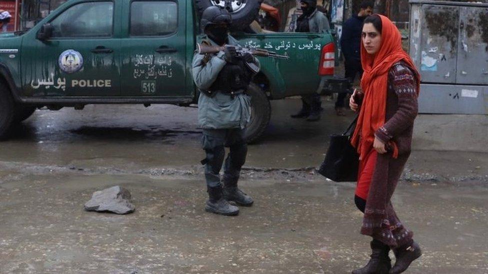 An Afghan woman walks near a security officer in Kabul