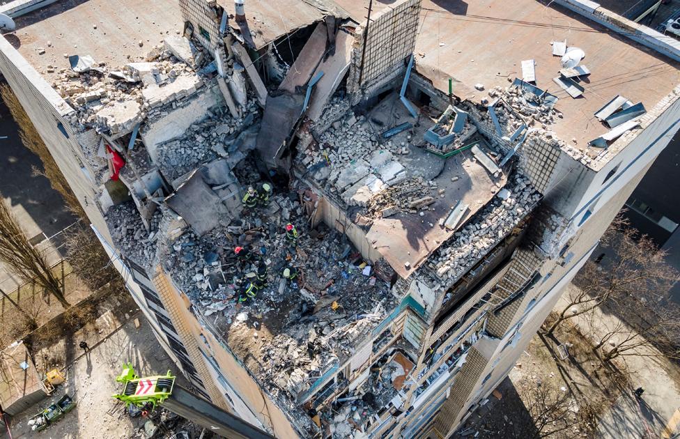 An aerial view shows firefighters working in the rubble of a residential building which was hit by the debris from a downed rocket in Kyiv on 17 March 2022