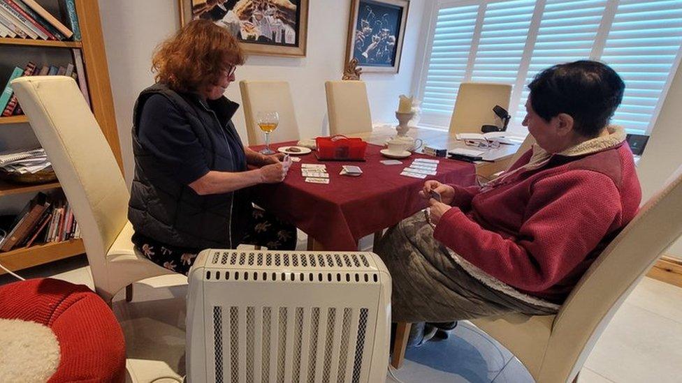 Two women play cards by an electric heater