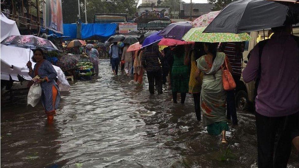 People trying to navigate the streets flooded with rain, umbrellas at hand.