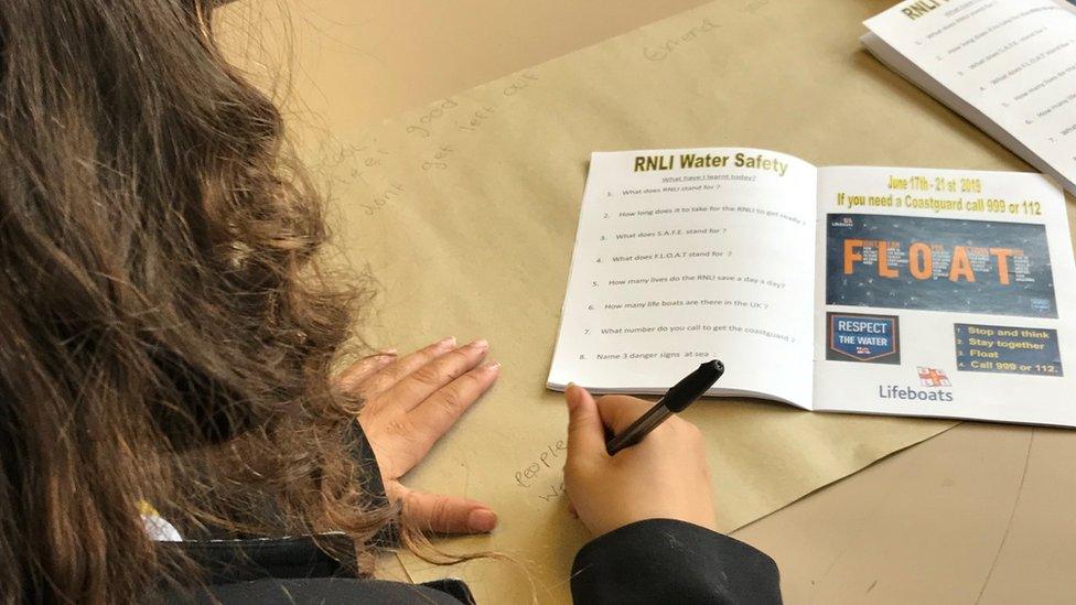 A girl writing on a water safety poster