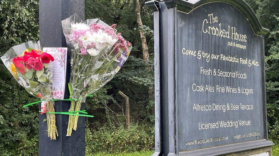 Flowers and a card left on signage outside the remains of The Crooked House pub near Dudley which has been demolished two days after it was gutted by fire.