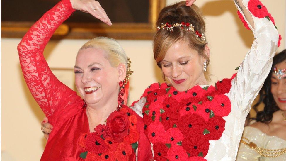 Two women in red dresses with their arms raised at the fashion show