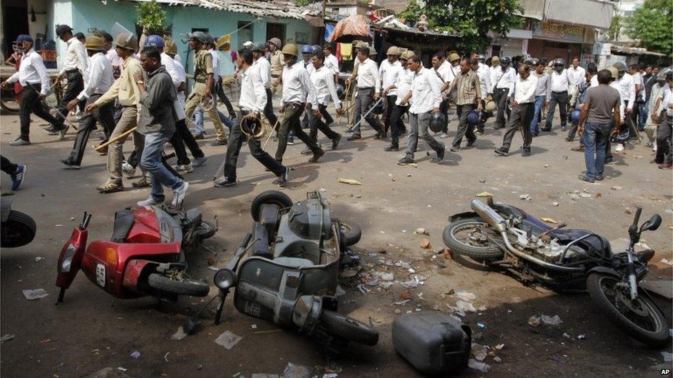 Indian policemen in plain clothes walk past vehicles damaged during a clash between two groups in Ahmadabad, India, Tuesday, Aug. 25, 2015.