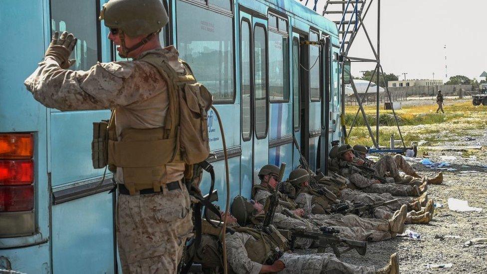 US soldiers rest as Afghan people wait to leave the Kabul airport in Kabul on August 16, 2021, after a stunningly swift end to Afghanistan's 20-year war.