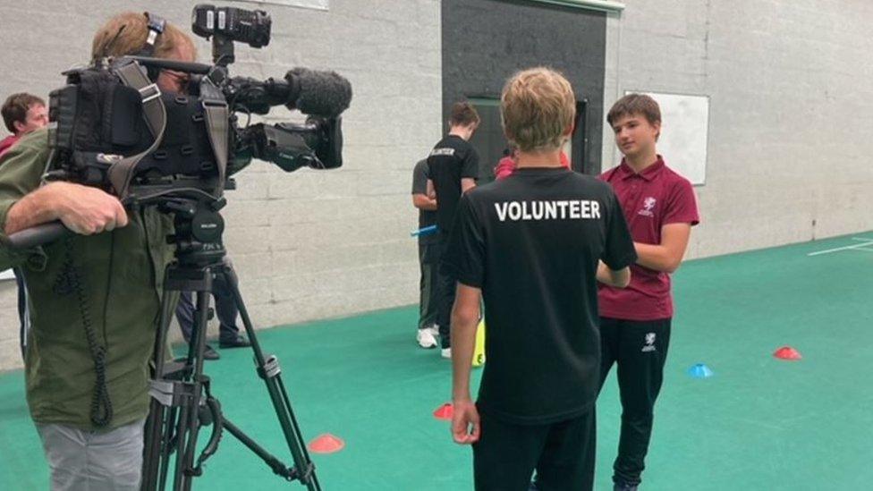 Matthew being filmed as he talks to a team member