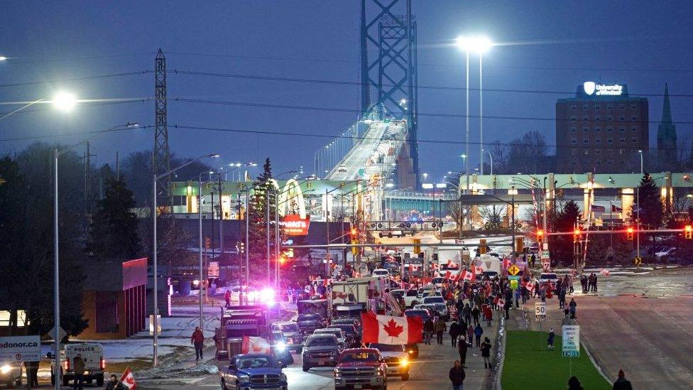 Night falls on the Ambassador Bridge with protesters in the foreground