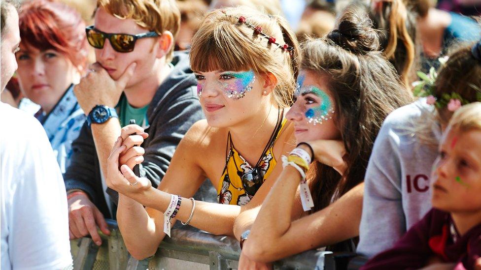 Female festival goers in a crowd wearing glitter on their faces.