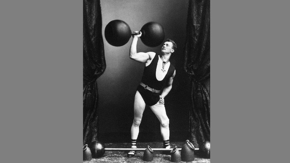 German strong-man Eugene Sandow (1867 - 1925) pictured with weights and an early form of kettlebell at his feet