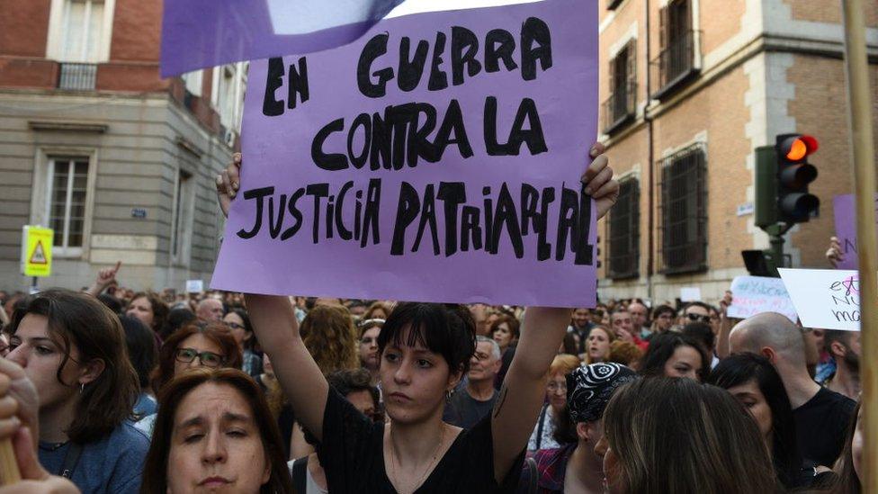 A woman holding a sign saying "in a war against patriarchal justice"