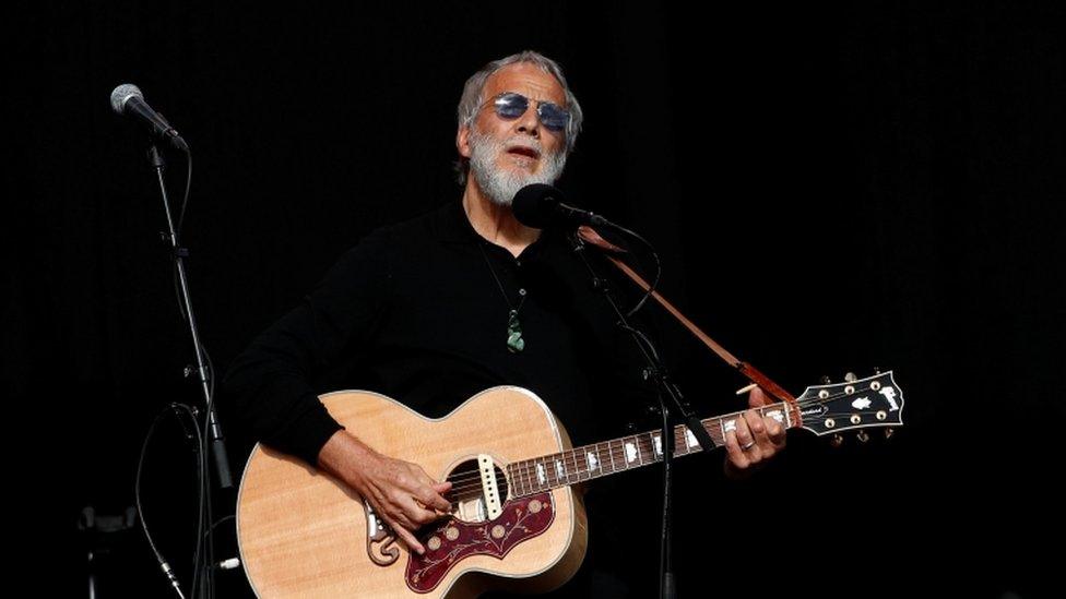 Cat Stevens playing guitar on stage at a memorial service for victims of the shooting on 29 March