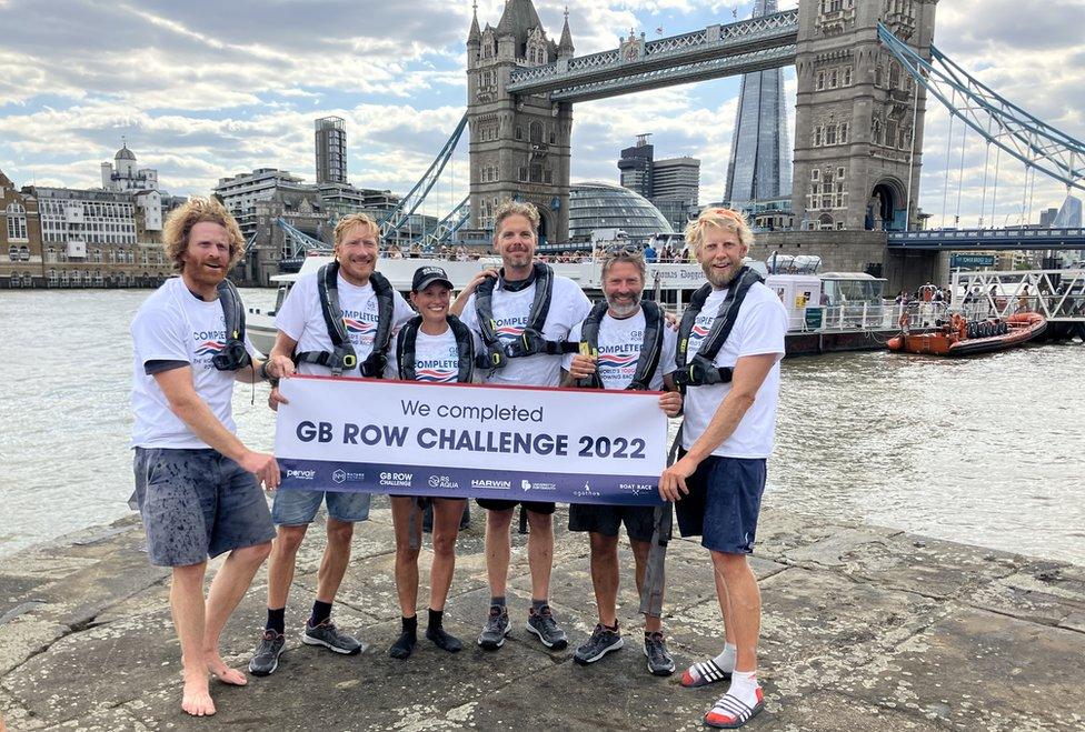 The team after completing the trip under Tower Bridge hold a sign saying "We completed GB Row challenge 2022"