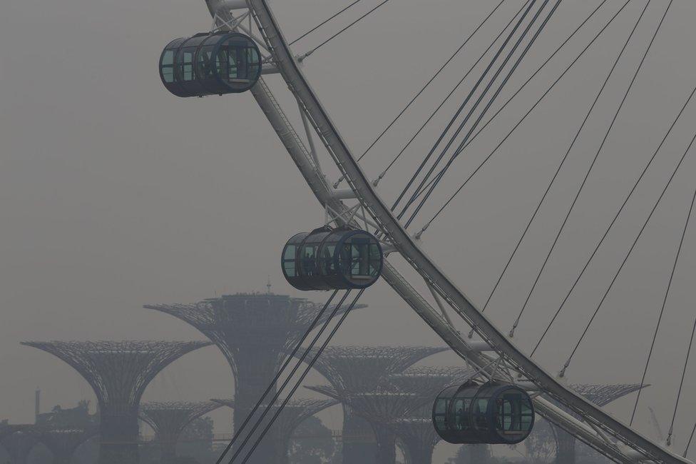 People look out from the Singapore Flyer Observation Wheel in the backdrop of the Gardens by the Bay shrouded by haze in Singapore 5 October 2015