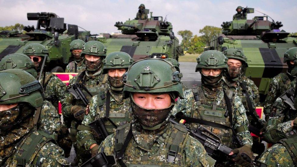 Taiwan soldiers bearing rifles stand at attention in front of tanks.